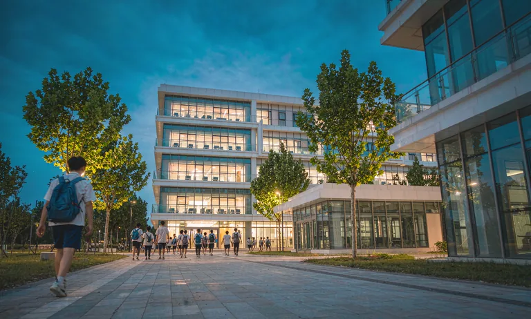A partner college campus at dusk with students walking towards a technical building