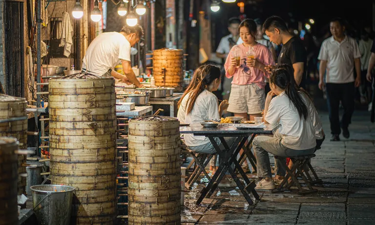 Students eating at a street-food stall on a wet evening