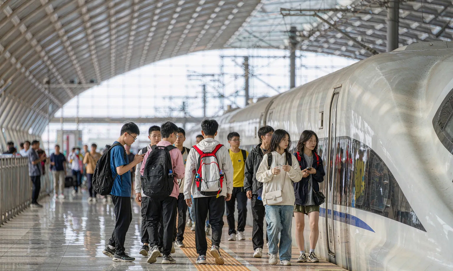 Teenage students with backpacks walking along a high-speed rail platform beside a train